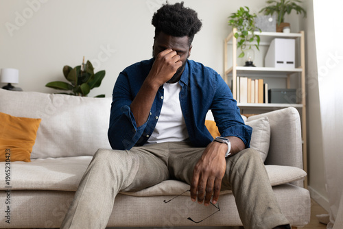 Φωτογραφία Tired Black man sitting on the sofa, having headache. Copy space.