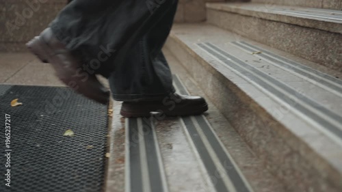 Closeup wet boots stepping mat, creator arriving on stone steps, rubber mat texture, slow deliberate pace, jeans hem brushing ground, rainy urban morning, tactile entrance detail