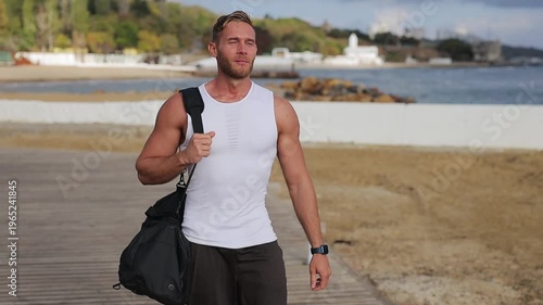 Young confident strong sporty athletic fit sportsman man wear sports clothes black bag stroll going to train warm up at sunrise sun dawn over sea beach outdoor on pier seaside in summer day morning