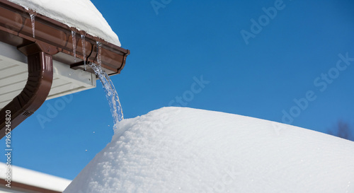 Snow-covered roof with melting snow flowing from the gutter  