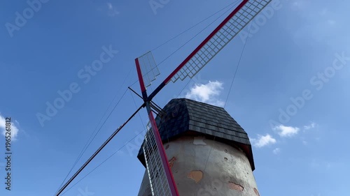 A close-up view of the top of an antique-style windmill as its blades slowly rotate in the wind.