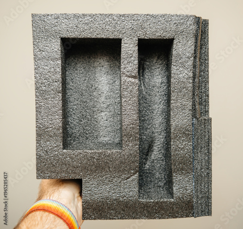 Close up POV of black polystyrene foam packaging insert with two rectangular compartments held by hand isolated on neutral background showing protective custom design