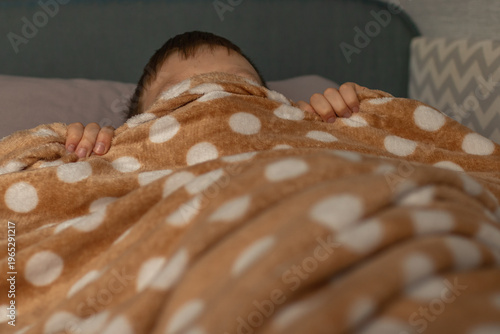 it's time to wake up for school. The boy covered his head with a blanket, not wanting to get up for school.