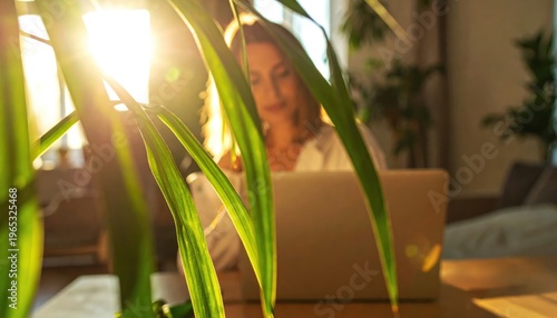 [Hybrid work concept] Woman working on laptop with sunlight shining through green plant leaves
