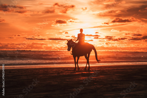 A majestic silhouette of a person riding a horse along the ocean shore during a vibrant, fiery sunset, creating a dramatic and serene scene.