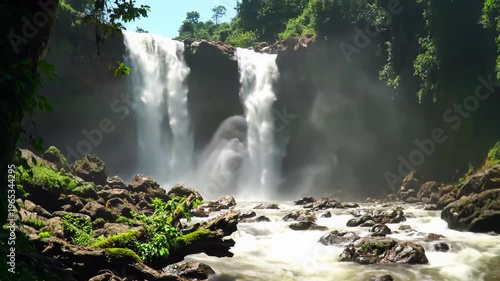 A majestic, powerful multi-stream waterfall cascades into a frothy riverbed in a lush primeval jungle, framed by an ancient tree branch. Awe-inspiring natural wonder
