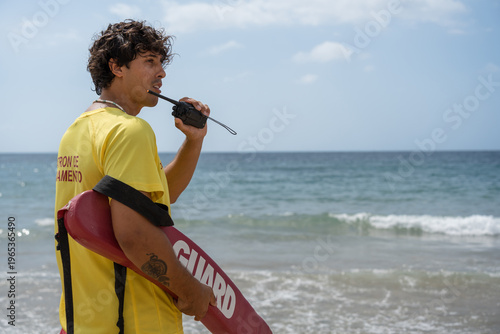Foto Lifeguard using walkie-talkie while patrolling beach on sunny day