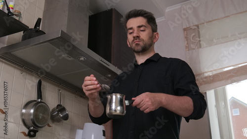 Photography Man in a black shirt preparing morning coffee with a jennycezve in his kitchen,