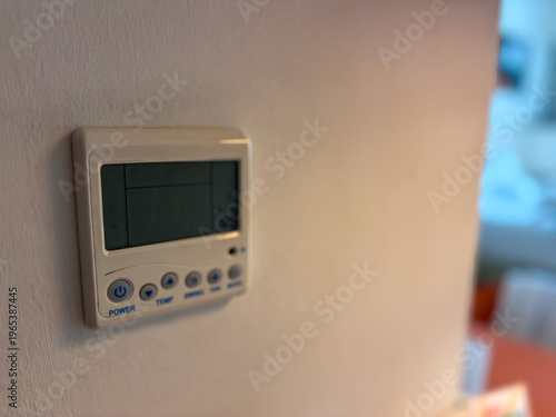 Close up of a wall mounted digital air conditioner remote control panel with LCD screen in a modern room