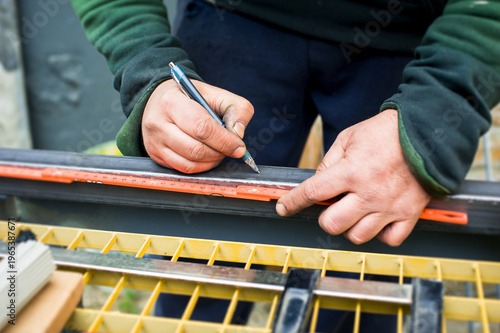 A worker focuses on measuring and marking a piece of material with a ruler and pencil at a bustling construction site under bright daylight. Attention to detail is key