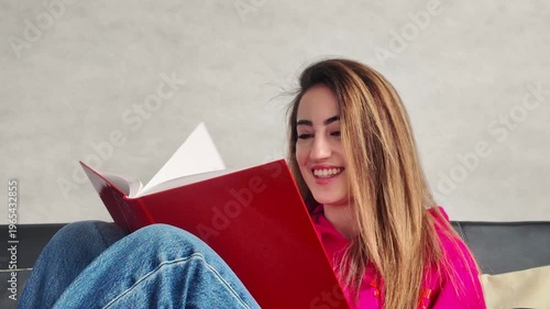 Young woman reading a red book on a couch
