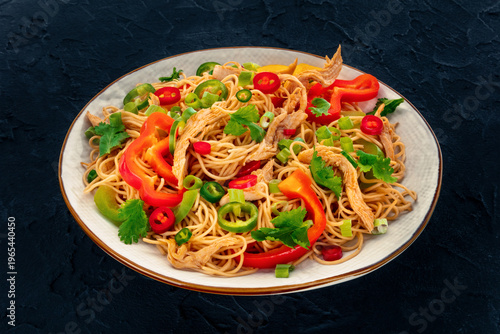 Chow Mein noodles with chicken and vegetables, on a black table