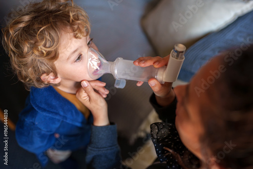 Photos Young child receiving respiratory medication with an inhaler and spacer mask for