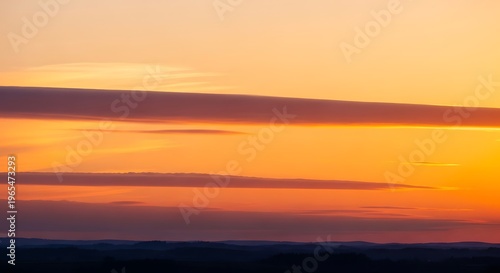 Sunset orange glow over landscape with dark cloud layers and vibrant evening light horizon scenery