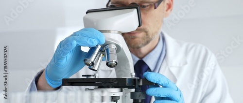 Schilderij op canvas Male scientist in white coat and blue gloves adjusting microscope, conducting pharmaceutical research in modern laboratory