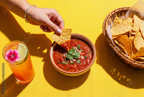 Fotografie hand dipping a mexican corn chip or tortilla chip in a spicy salsa dip, top view