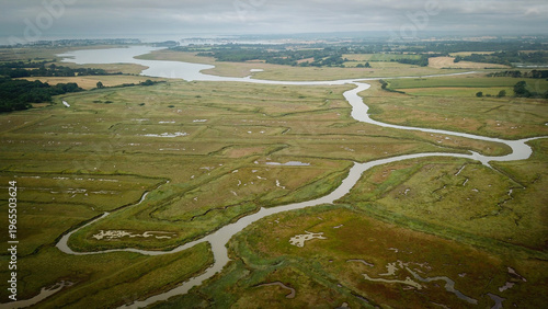 Aerial view of winding waterways carve intricate paths through the vibrant green marshes, a tapestry of nature's artistry unfolding beneath a serene sky, Ambon, Brittany, France.