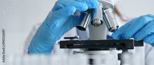 Foto Close up of scientist's gloved hands adjusting microscope, conducting research in laboratory with test tubes containing blue liquid in background