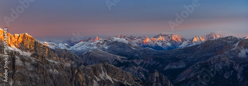 Aerial view of the rugged Alps mountains, snow-dusted peaks catch the warm glow of the rising sun, contrasting sharply with the cool shadows nestled in the valleys, Veneto, Italy.