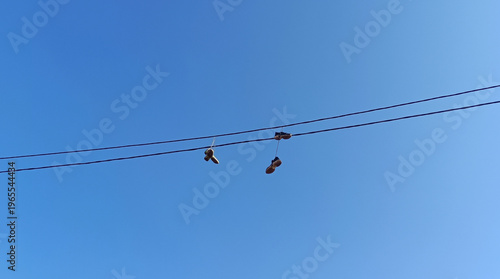 Urban Shoefiti Featuring Sneakers Hanging from an Overhead Power Line Against a Clear Blue Sky