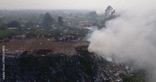Aerial close-up fly over view. Burning rubbish causing greenhouse gas, contributor to climate change.  Extreme Poverty. People living alongside dumpsite struggling to survive through waste picking.