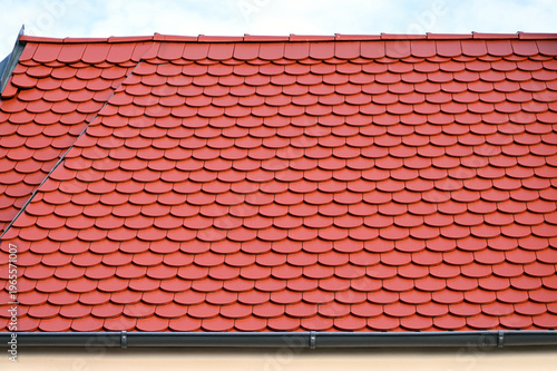Sloped red clay tile roof. round beaver tail edge. gray Zink metal flashing. ridge tiles at the top. metal gutter and clamps. modern home building materials. residential building construction.