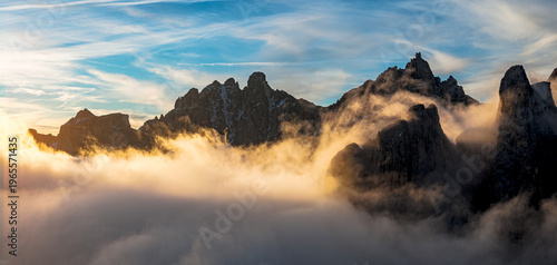 Aerial view of jagged peaks in Badia valley pierce through a sea of swirling mist under a sky streaked with dawn's light, Trentino-Alto Adige, Italy.