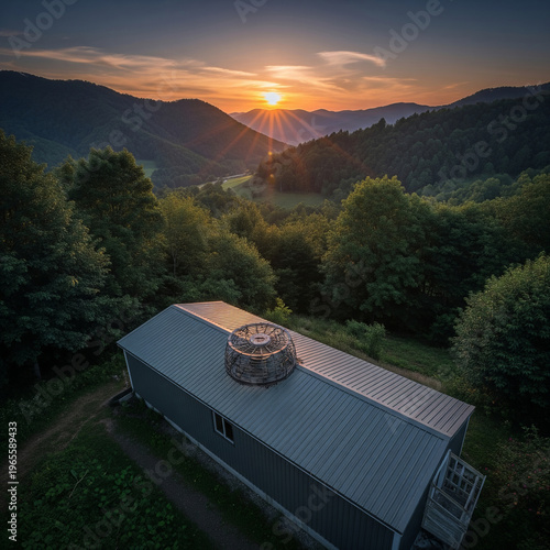 Aerial view of rural house with circular rooftop structure in lush green mountain valley at sunset