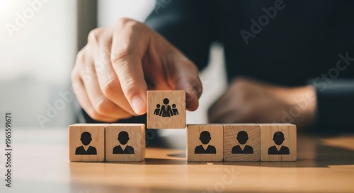 Hand placing wooden block with people icon on stack, representing team building and human resources