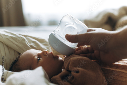Feeding cute newborn baby with bottle on cozy blanket, close up. Mother or father feeding sweet little infant with formula, space for text. Adoption. Child health and skin care concept