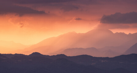 Silhouettes of Alpine mountains at colorful sunset in summer in Slovenia. Landscape with mountain ridges in fog, golden sunlight and clouds in the evening. Alps. Nature. Hills in sunlight. Scenery