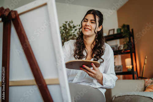 Foto Young woman enjoying painting on canvas at home