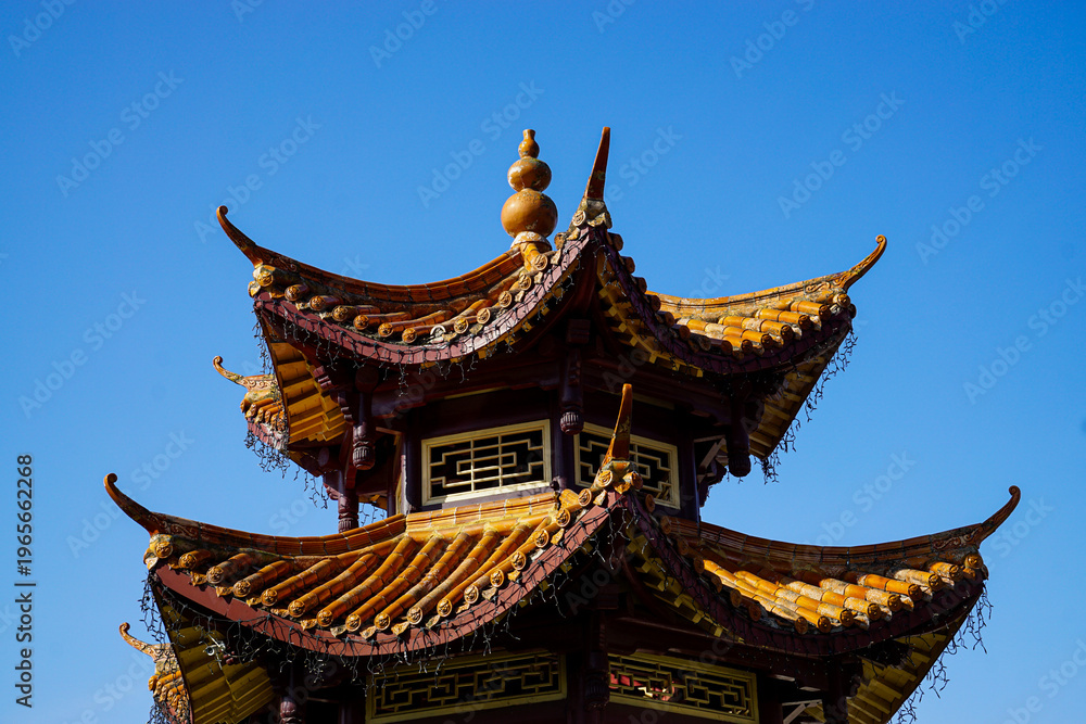 Fototapeta premium Detailed view of a traditional Chinese pagoda with ornate curved roofs and ceramic tiles under a clear blue sky, ideal for travel, culture, and architectural design use.