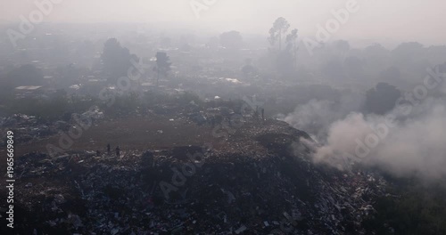 Aerial close-up panning view. Burning rubbish causing greenhouse gas, contributor to climate change.  Extreme Poverty. People living alongside dumpsite struggling to survive through waste picking.