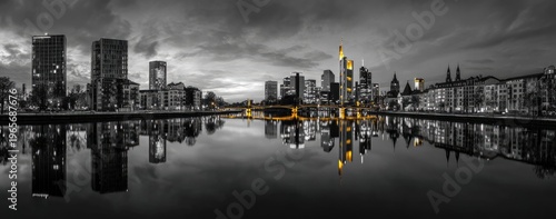 A grayscale skyline shot reflecting in water, with golden accents, under an overcast sky