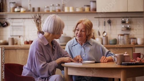 Positive senior women looking through photo album, sharing joyful memories