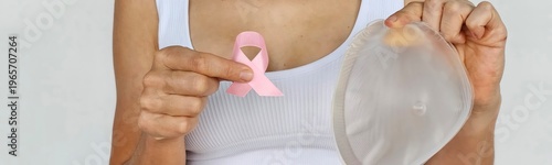 A woman holds a silicone breast implant and a pink ribbon to symbolize breast cancer awareness
