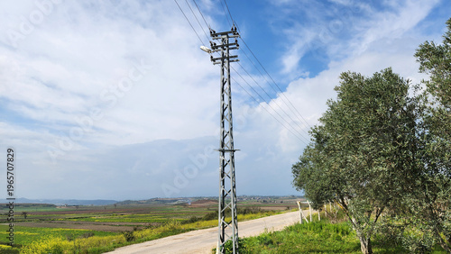 A metal electricity pole with a streetlight along a rural roadside