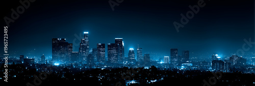 A panoramic cityscape at night, illuminated with blue lights. Skyscrapers and buildings reach toward the dark sky. The city lights twinkle