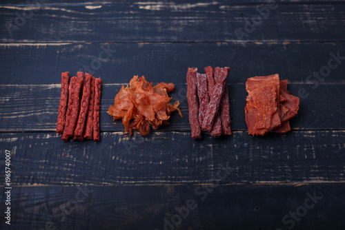 Dry salmon fish, chicken, red beef sticks and pork slices. Jerky meat on black wooden background. No brand, product presentation. Copy space, top view