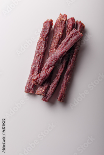 Dry beef sticks heap, jerky meat pile on white background. Copy space, top view. Advertising banner, template. Product presentation. Vertical shot
