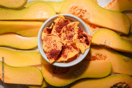 Autumn superfood. Raw and dehydrated crispy pumpkin chips in bowl and white background. Product presentation