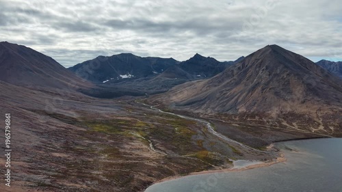 Drone footage shows drift over Rumilet Bay mountain valley in Chukotka. River delta and tundra slopes under overcast autumn sky. Remote travel landscape for cinematic documentary and tourism use