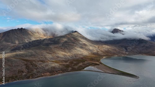 Aerial drone footage drifting over rugged ridges and lake at Rumilet Bay, Chukotka. Slow drift reveals vast tundra slopes and calm water. Cloudy autumn morning supports adventure travel mood