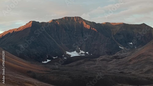 Drone flyover at Rumilet Bay in Chukotka during autumn evening in September. Drone pans right to reveal new ridgelines and valleys. Mountain wall encloses a quiet basin with lingering snow