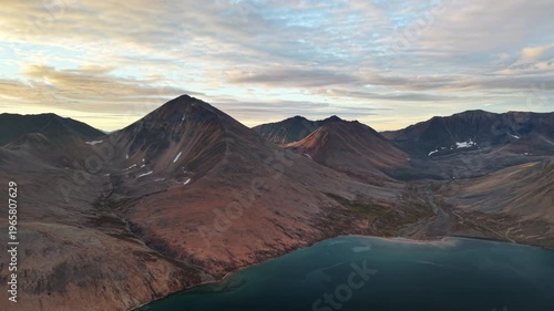 Aerial drone footage drifts above Rumilet Bay, revealing valleys and mountain ridges in Chukotka. Soft autumn evening colors warm the tundra. Scenic coastline feels remote and cinematic