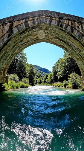 Stone Arch Bridge Over Turquoise River With Lush Green Trees And Bright Blue Sky