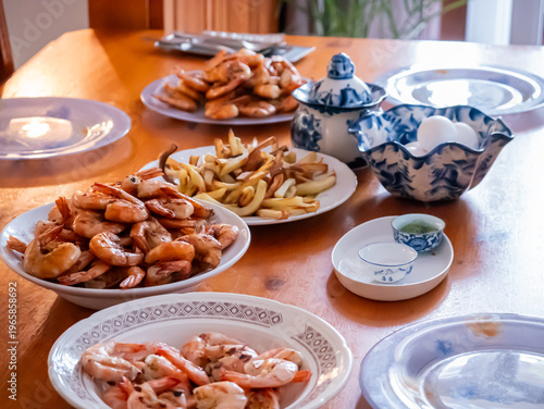 Fried shrimp served on white plates on wooden dining table. Delicious seafood dinner prepared for family gathering. Traditional meal setting with lemon and porcelain dishware.