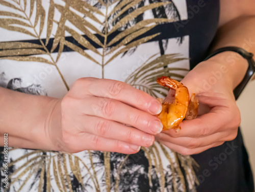 Woman peeling cooked shrimp. Culinary preparation of seafood snack. Hands cleaning crustacean before eating meal. Gastronomy, healthy protein food and kitchen activity concept in home setup.