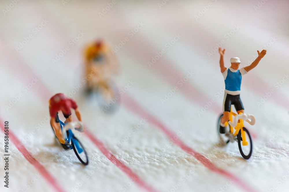 Obraz premium Miniature Cyclists Representing Corporate Success and Financial Growth with the leader raising his arms in victory